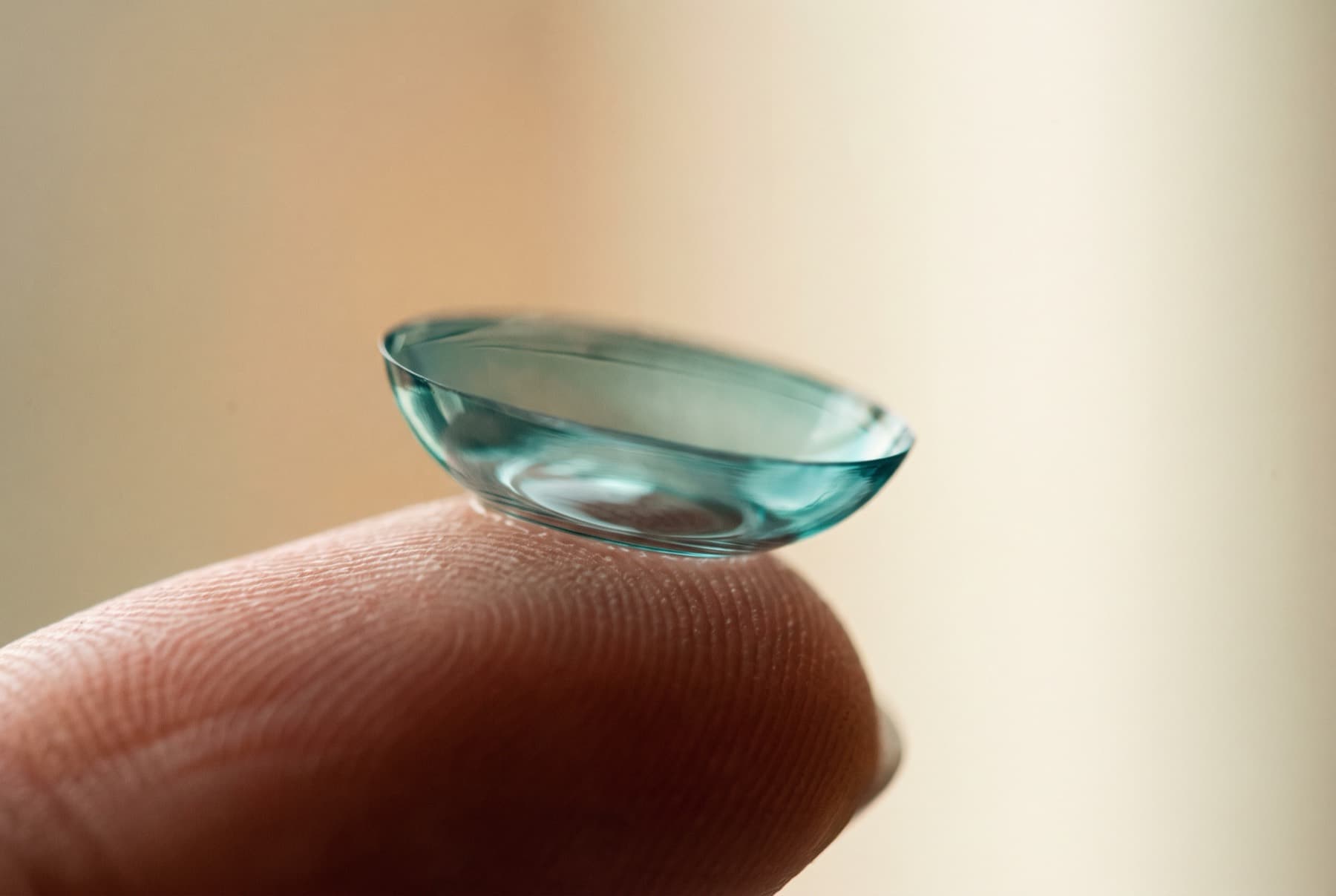 A specialty scleral contact lens balanced on a fingertip in soft light